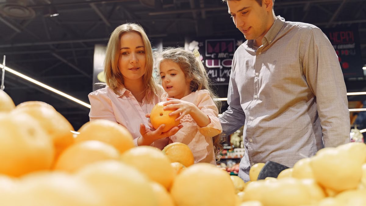 Parents and child selecting fresh oranges together at the supermarket. Captures family bonding and healthy shopping.